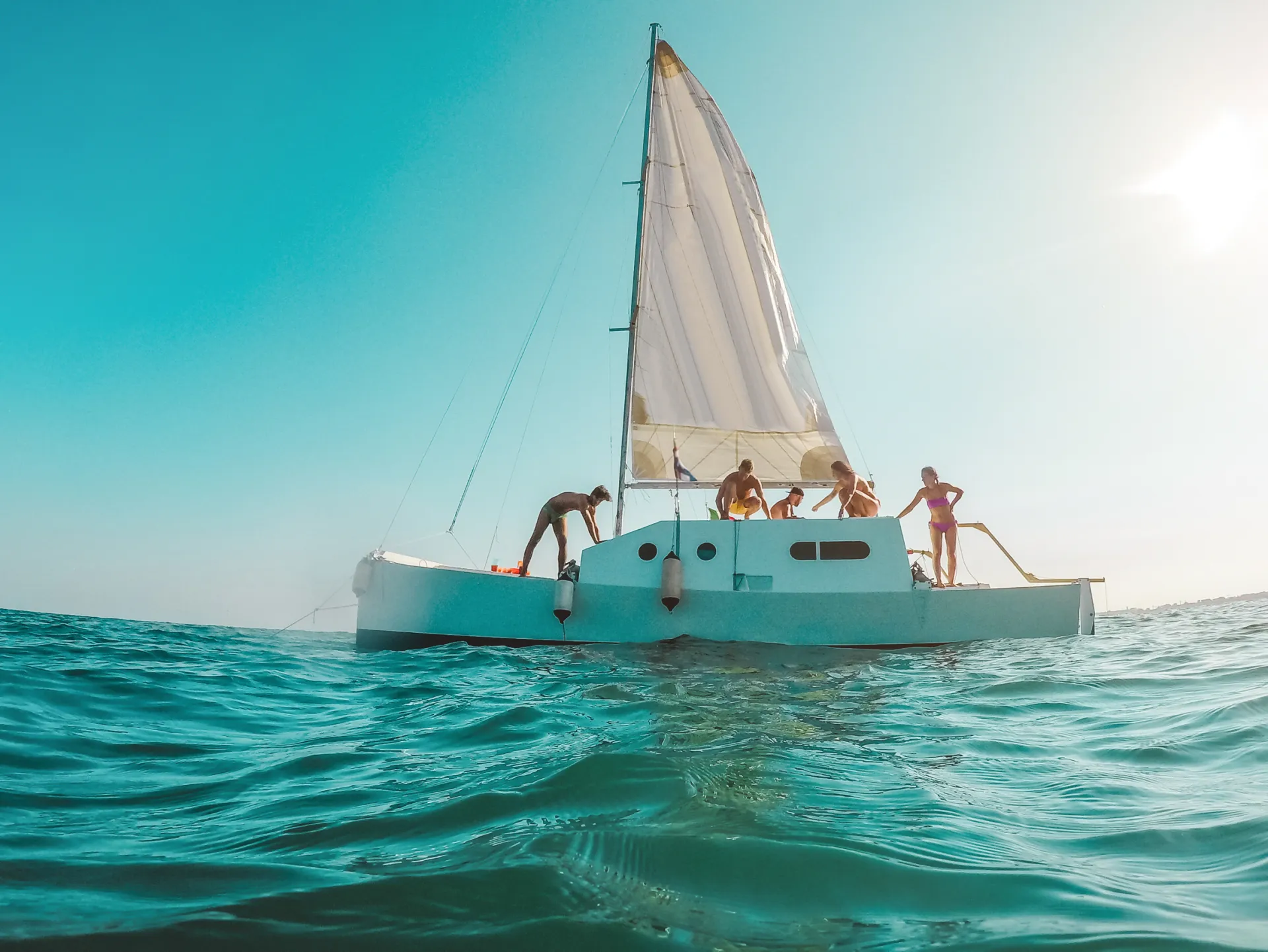 Groupe de personnes sur un voilier blanc naviguant sur une mer turquoise sous un ciel bleu clair et ensoleillé
