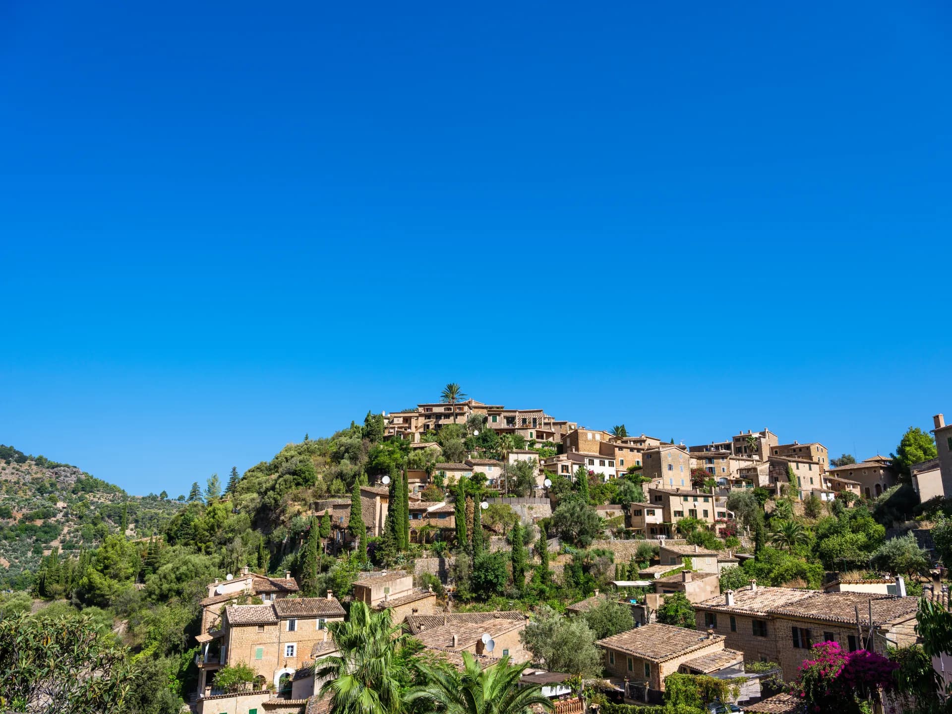Village méditerranéen perché sur une colline verdoyante sous un ciel bleu éclatant, maisons en pierre aux toits de tuiles